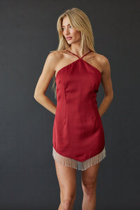 A blonde model wearing a red halter-neck mini dress with a fringe hem, posed against a dark gray studio background.