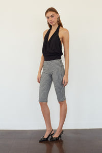 A woman modeling black and white gingham checkered capri pants with a black halter top, standing against a plain white wall.