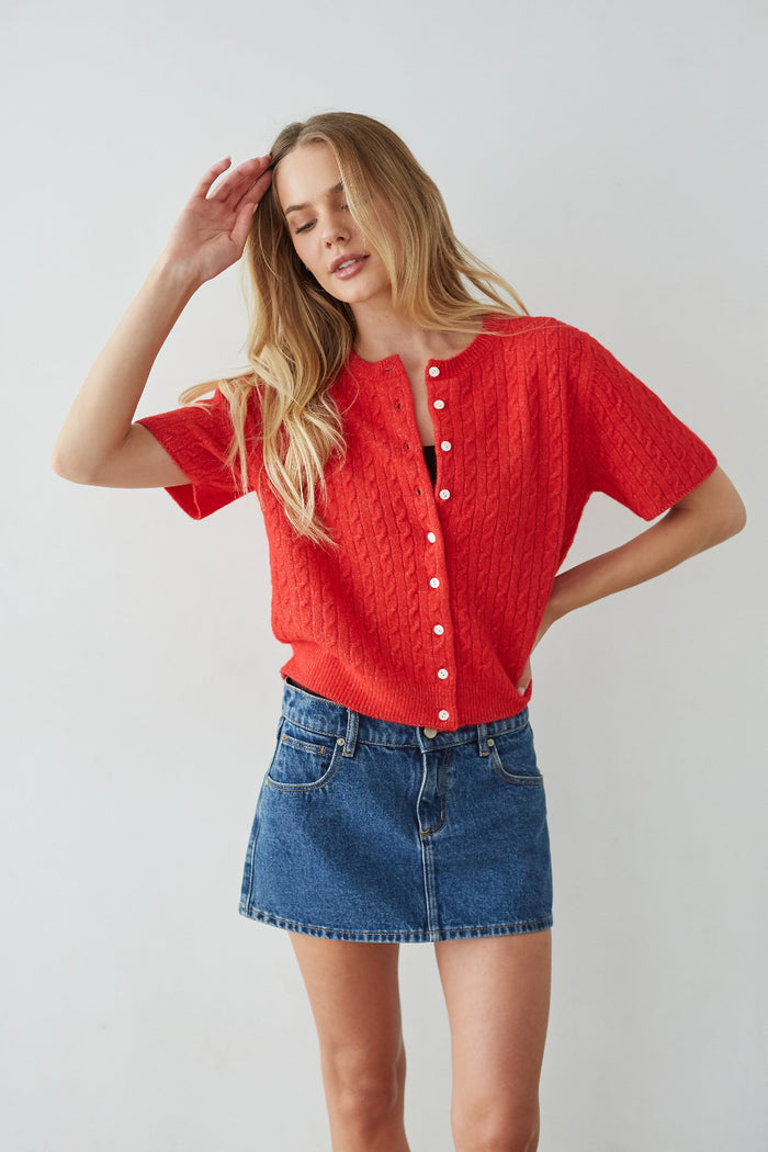 Woman wearing a red knitted top and blue denim skirt against a white background
