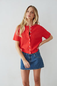 Woman wearing a red textured shirt and blue denim skirt against a plain background