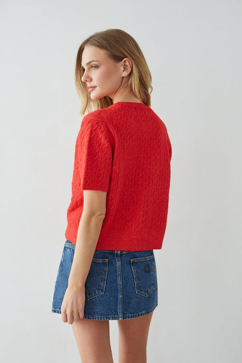 Woman wearing a red sweater and blue denim skirt on a light gray background