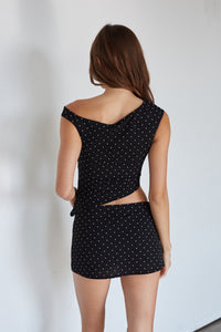 Woman wearing a black polka dot dress with cut-out design on a plain background