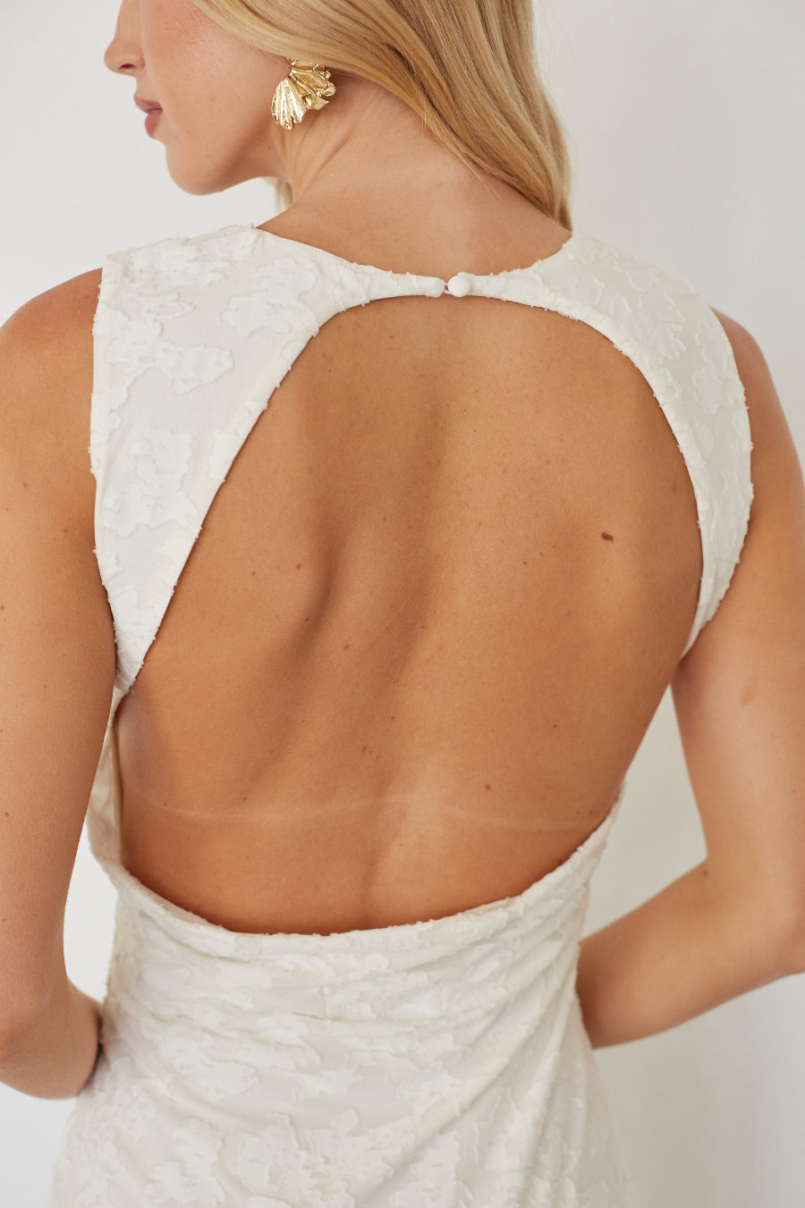 Woman wearing a white dress with an open back against a plain background