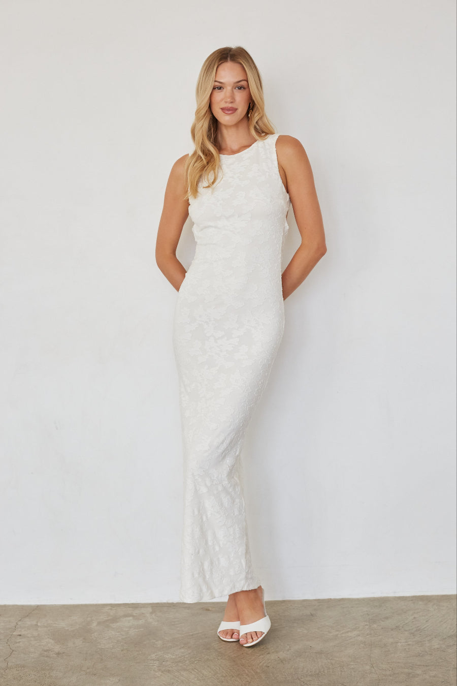 Woman wearing a white sleeveless dress against a plain background