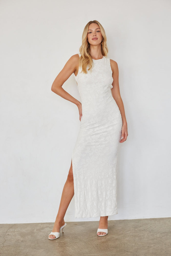 Woman wearing a white sleeveless dress with a slit on a plain background