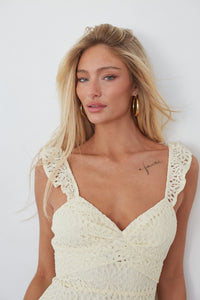 Woman wearing a white crochet dress against a plain background