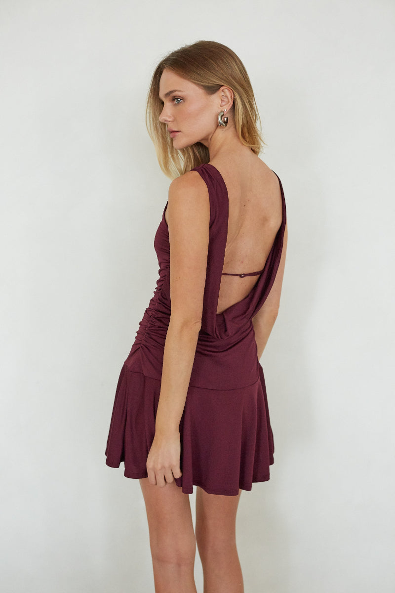 Woman wearing a burgundy dress with cut-out back on a white background