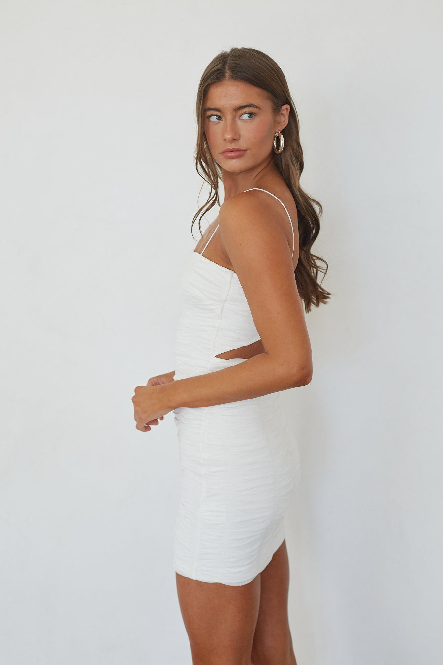 Model wearing the Lizeth Ruched Bodycon Mini Dress in white, side profile view