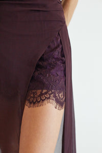 Close-up of a dark plum wrap skirt with a thigh-high side slit, featuring a sheer mesh panel and a matching lace insert on the inner side.