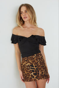 Woman wearing a black off-shoulder top and leopard print skirt against a white background