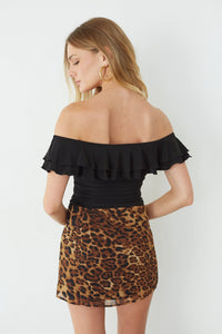 Woman wearing a black off-shoulder top and leopard print skirt on a white background