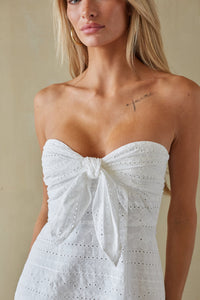 Woman wearing a strapless white dress with a bow detail against a neutral background
