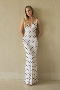 white-image | Woman wearing a white dress with black polka dots against a beige wall.