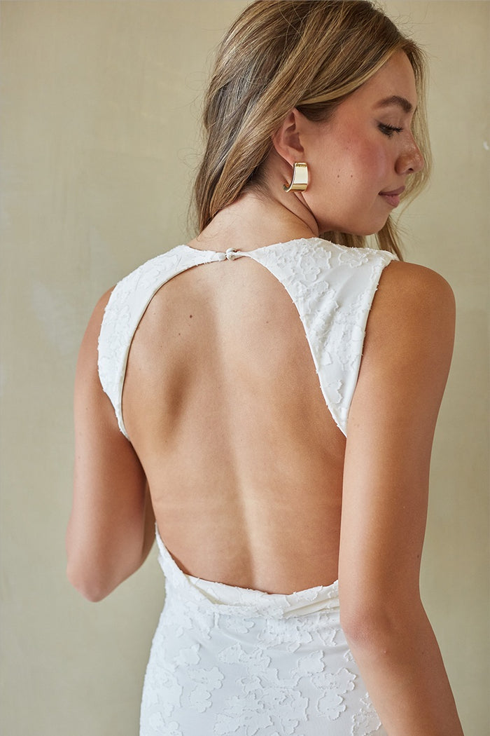 Woman wearing a white lace dress with an open back against a beige background