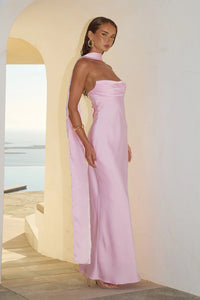 Woman wearing a pink strapless dress standing against a white wall with a blurred outdoor background.