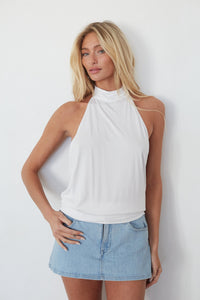 Woman wearing a white halter top and denim skirt against a plain background