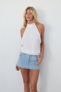 Woman wearing a white halter top and denim skirt against a plain background