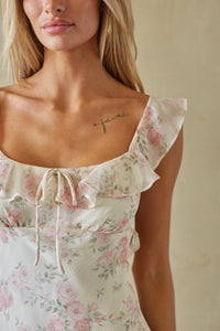 Woman wearing a floral dress with ruffled shoulders against a neutral background