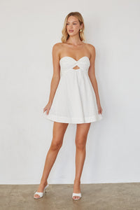 Woman wearing a white strapless dress with a cutout design against a plain background