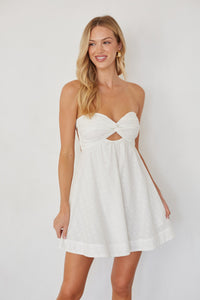 Woman wearing a white strapless dress with cut-out design on a plain background