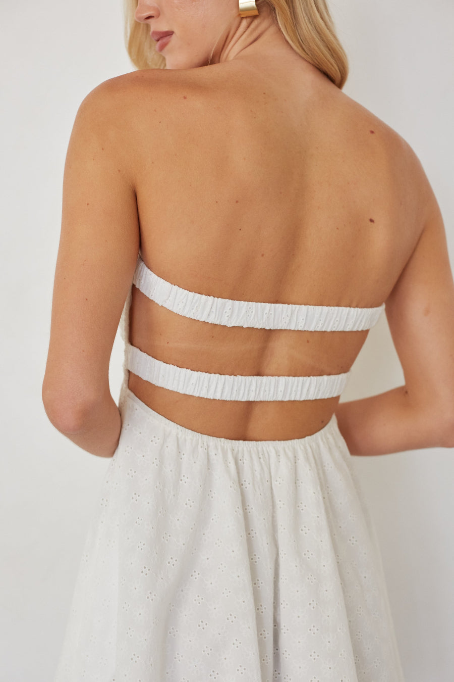 Woman wearing a white dress with a sheer back panel against a plain background