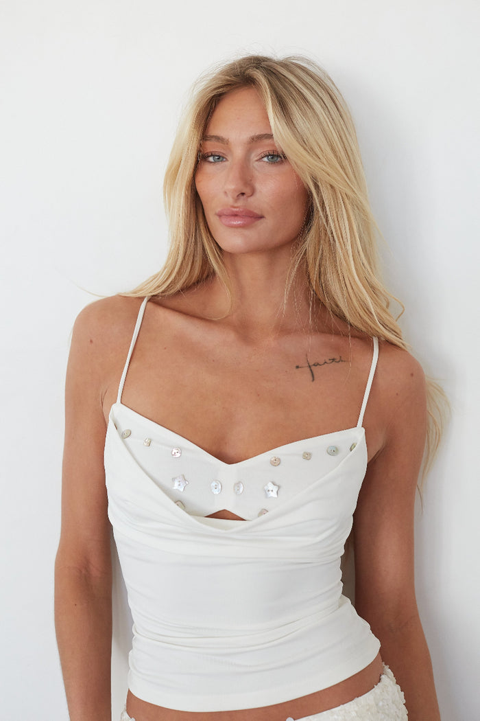 Woman wearing a white top with thin straps against a plain background