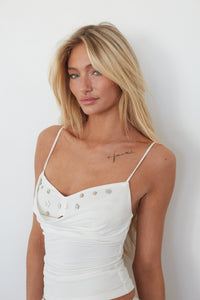 Woman wearing a white tank top against a plain background