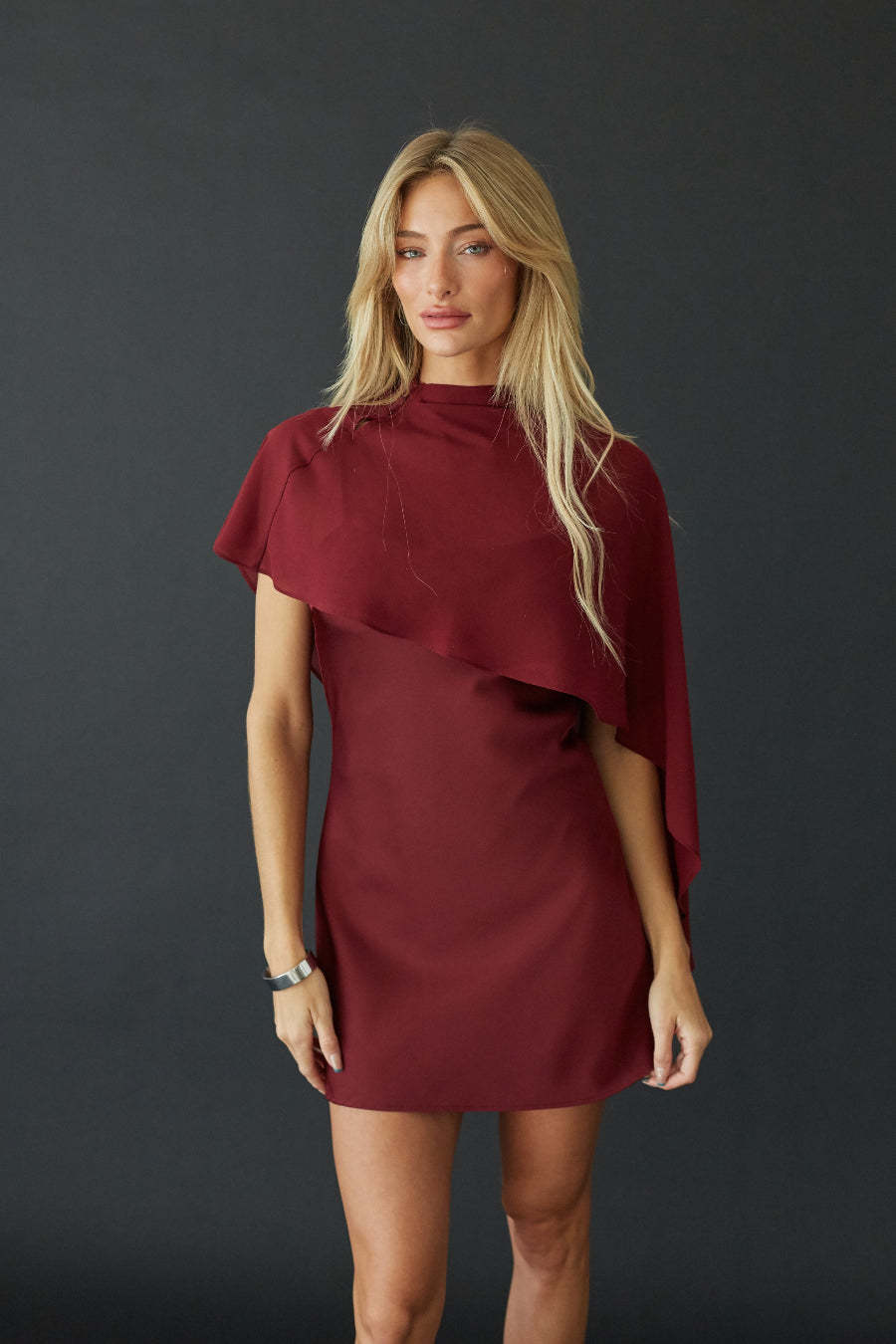 Burgundy satin mini dress with sheer cape, front view showing cape drape on model
