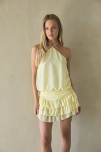 yellow-image | Woman wearing a light yellow halter neck dress against a plain background