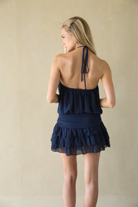 Woman wearing a navy blue halter neck dress with ruffled layers on a beige background