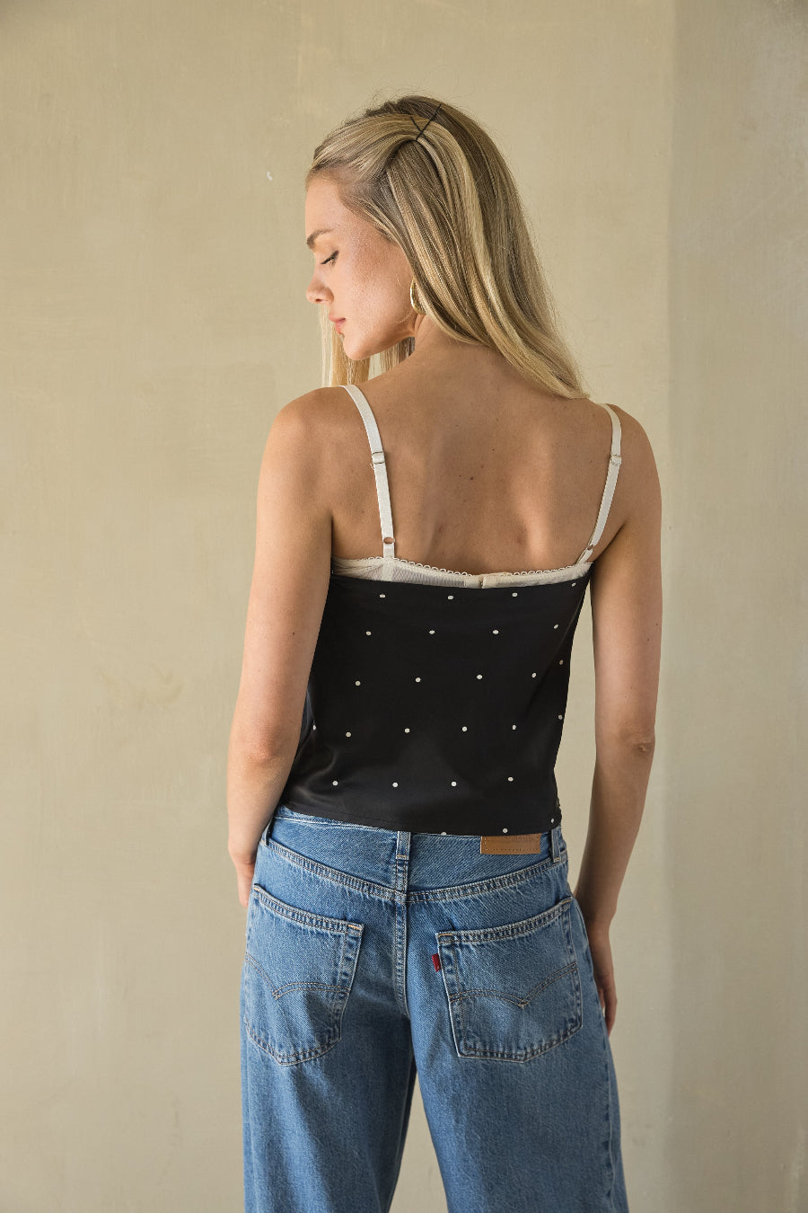 Woman wearing a black polka dot top and blue jeans against a beige background