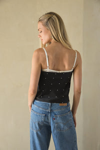 Woman wearing a black polka dot top and blue jeans against a beige background