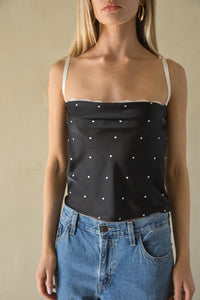 Woman wearing a black polka dot top and blue jeans against a beige background