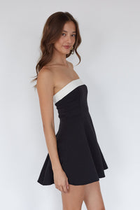 Woman wearing a black and white strapless dress against a plain background