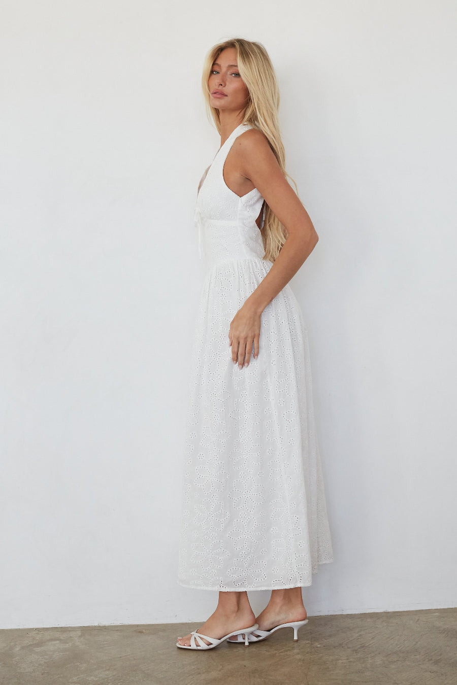 Woman wearing a white dress standing against a plain white wall.