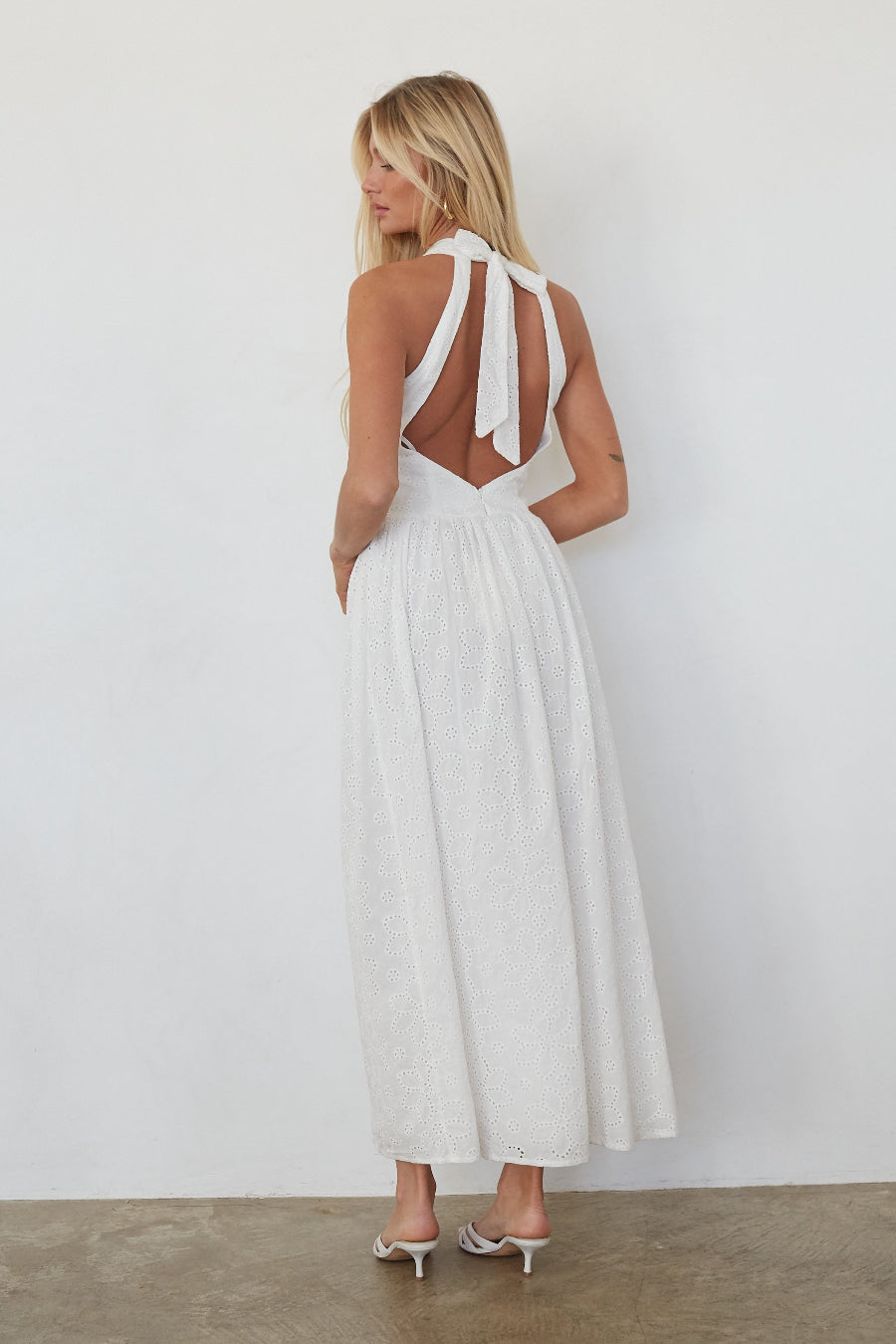 Woman wearing a white dress with cut-out back design against a plain background