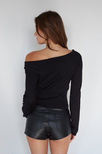 Woman wearing a black off-shoulder top and black leather shorts against a white background