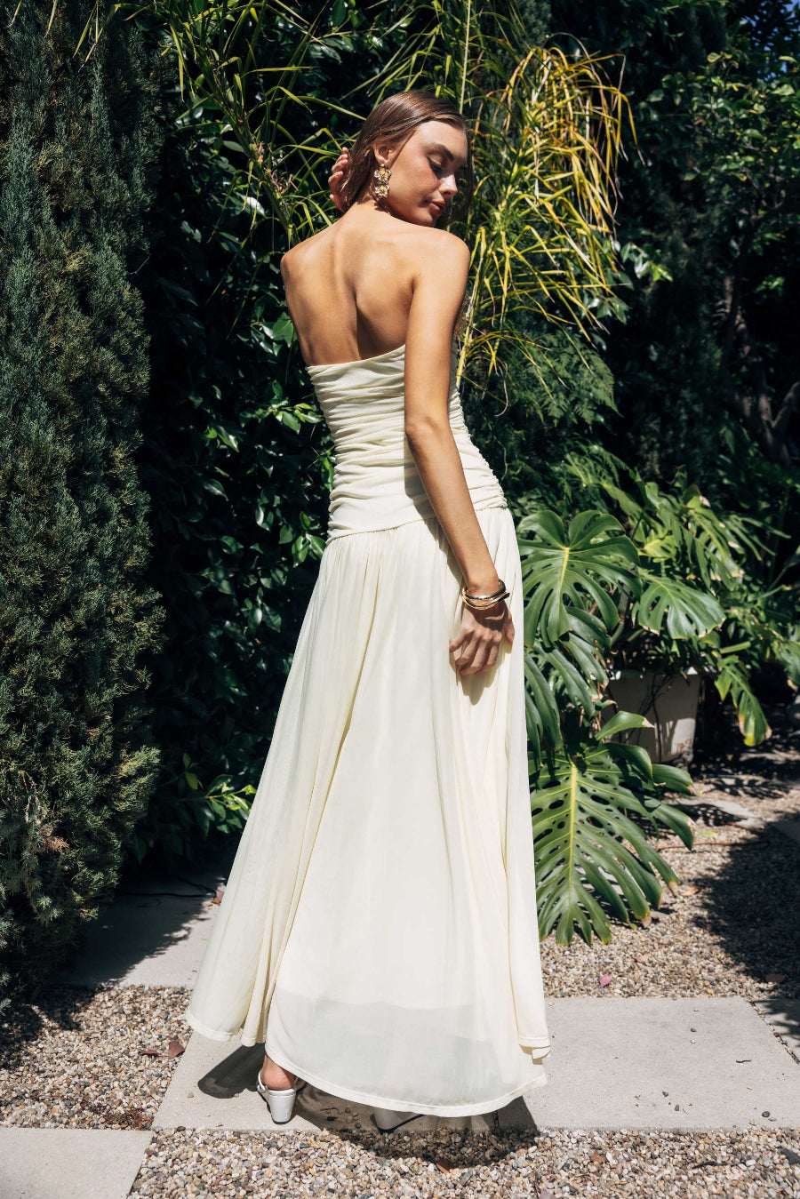 Woman in a yellow strapless dress standing outdoors with greenery in the background