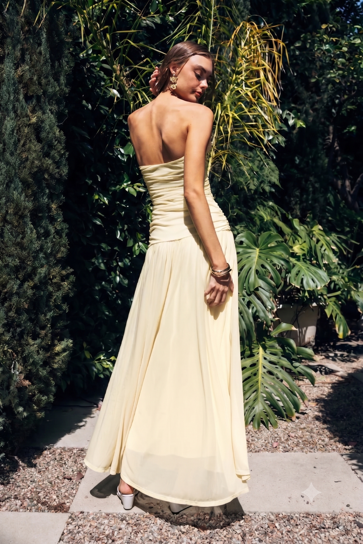Woman in a yellow strapless dress standing outdoors with greenery in the background