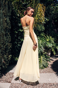 Woman in a yellow strapless dress standing outdoors with greenery in the background