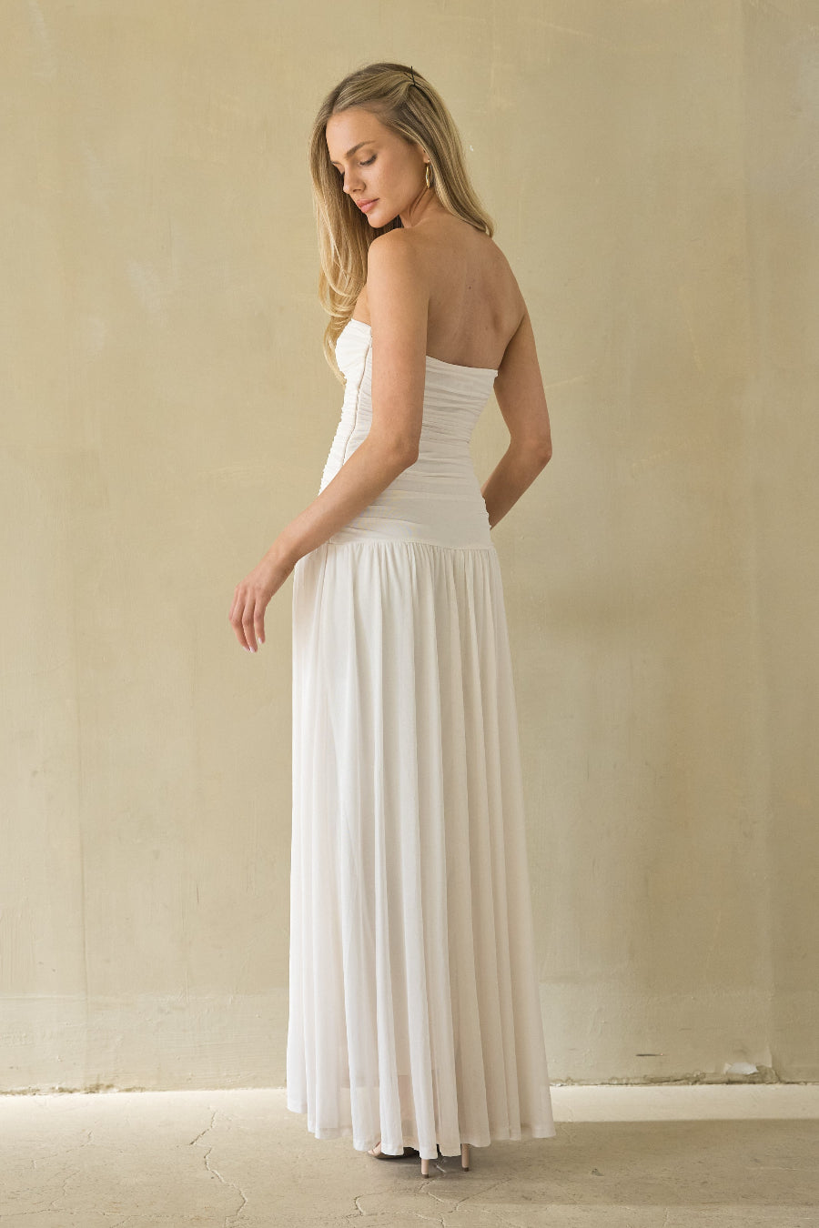 Woman wearing a white strapless gown against a plain background