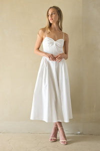 Woman wearing a white dress with a bow detail in a minimalistic setting