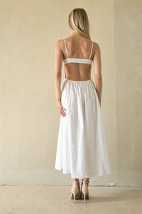 Woman wearing a white dress with thin straps and open back in a minimalistic setting.