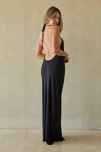 Woman wearing a black open-back dress against a beige wall.