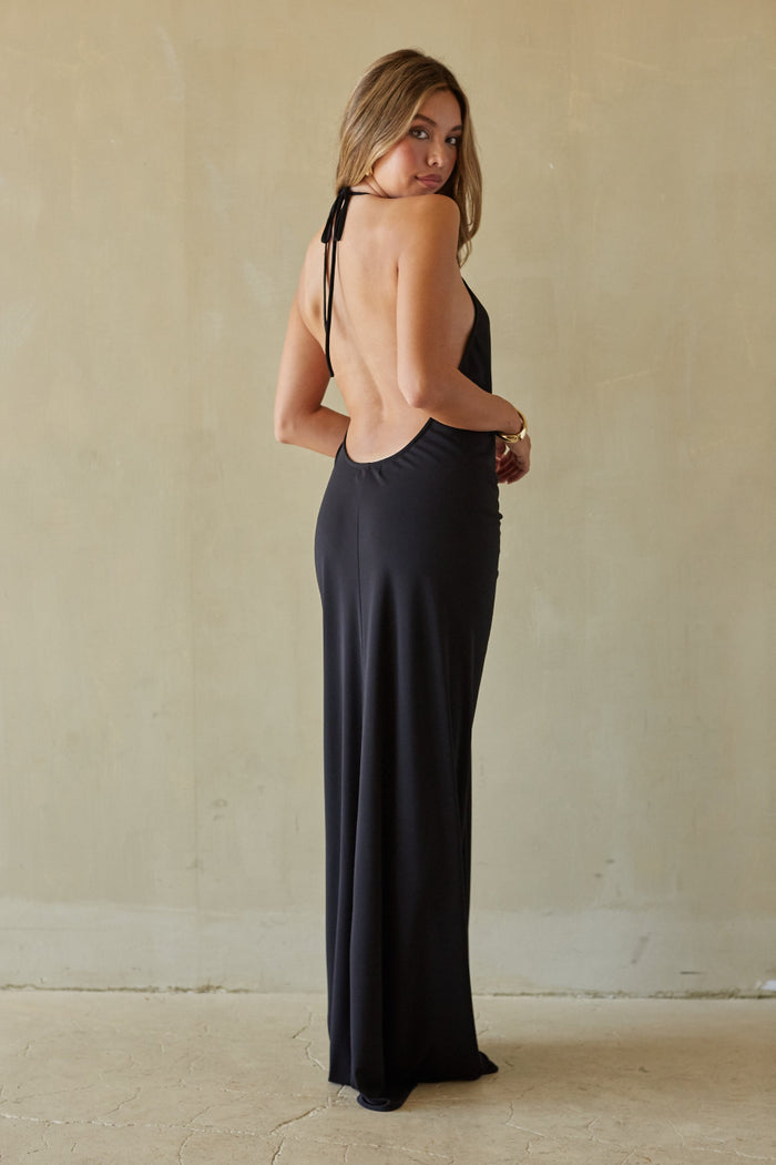 Woman wearing a black open-back dress against a beige wall.