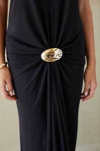 Black dress with a gold embellishment on a neutral background