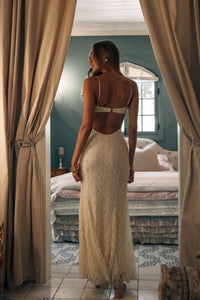 Woman in a beige dress standing in a bedroom with curtains open
