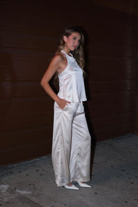 Women standing to show off the side view of a matching white satin set in front of a dark wall.