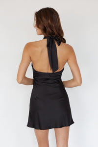 Woman wearing a black halter neck dress with a bow detail on a white background