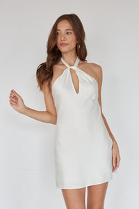 Woman wearing a white halter neck dress against a plain background
